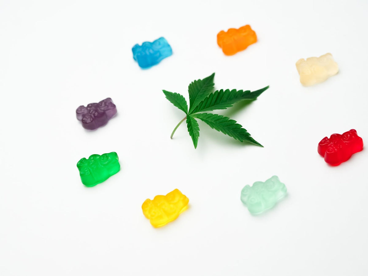 Vibrant assortment of gummy candies surrounding a cannabis leaf, creatively displayed against a white background.